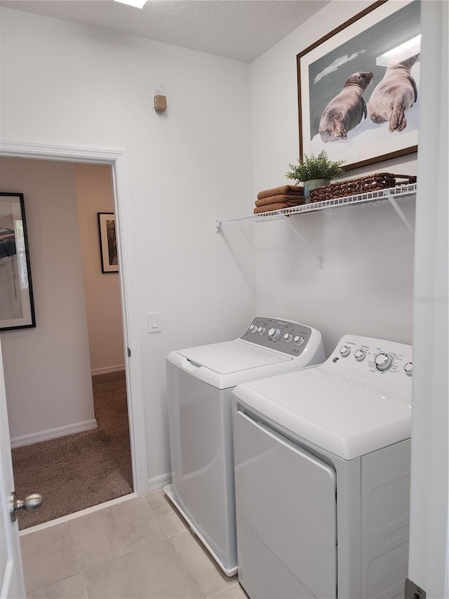 washroom featuring a textured ceiling, light tile patterned flooring, laundry area, baseboards, and washer and dryer