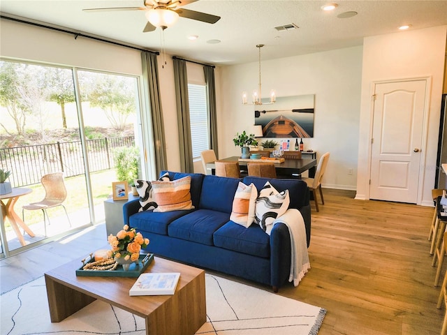 living room featuring recessed lighting, visible vents, light wood-style floors, baseboards, and ceiling fan with notable chandelier