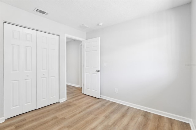 unfurnished bedroom featuring a textured ceiling, a closet, and light wood-type flooring