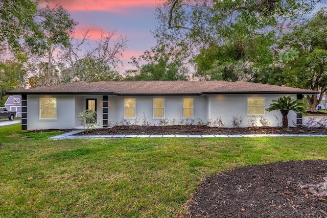 single story home with stucco siding, a lawn, and roof with shingles