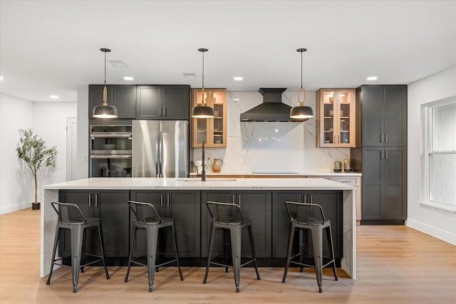 kitchen with a sink, appliances with stainless steel finishes, a large island, decorative backsplash, and wall chimney exhaust hood