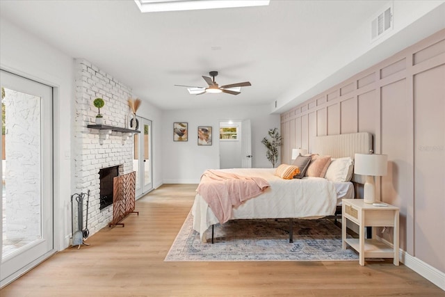 bedroom with light wood-type flooring, access to outside, a fireplace, and visible vents