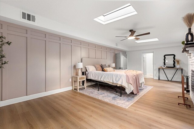 bedroom with a skylight, visible vents, a ceiling fan, light wood-type flooring, and a decorative wall