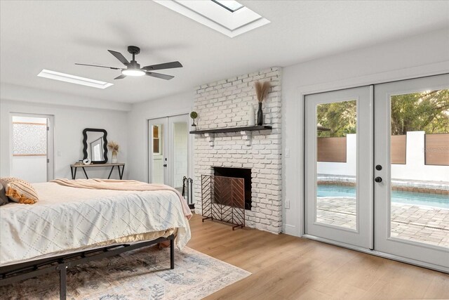 bedroom with french doors, a fireplace, light wood-style flooring, ceiling fan, and access to outside