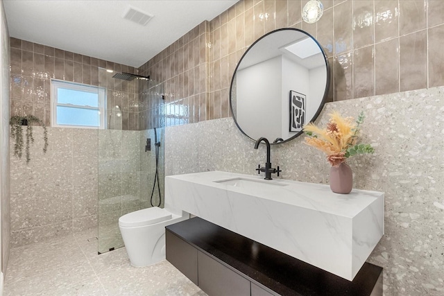 bathroom with a walk in shower, toilet, visible vents, vanity, and tile walls