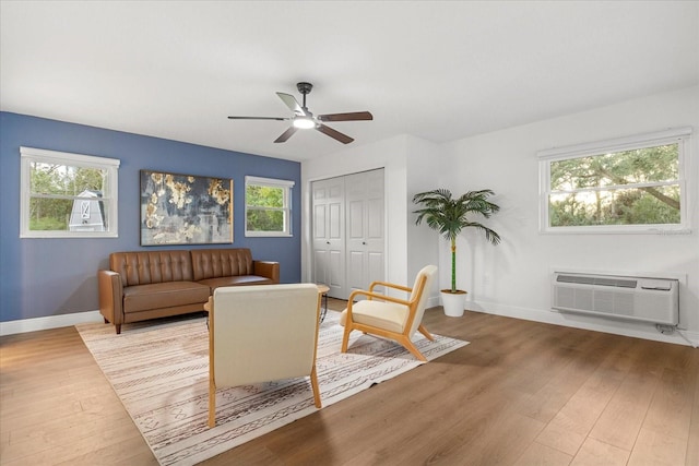 living area featuring a wall mounted AC, wood finished floors, a ceiling fan, and baseboards