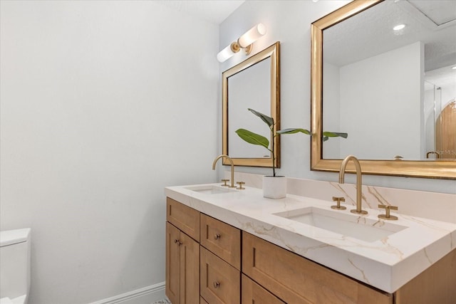 full bathroom featuring toilet, double vanity, baseboards, and a sink