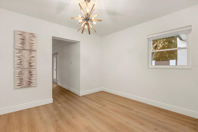 empty room with an inviting chandelier, baseboards, and light wood-style floors