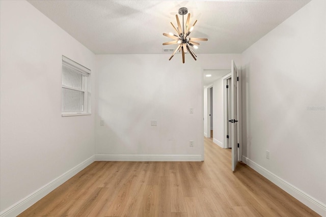 spare room featuring a notable chandelier, light wood-style floors, visible vents, and baseboards