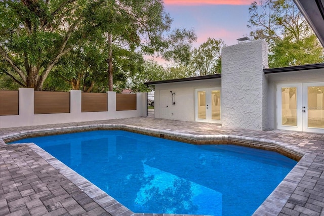 pool at dusk featuring a patio area, fence, a fenced in pool, and french doors