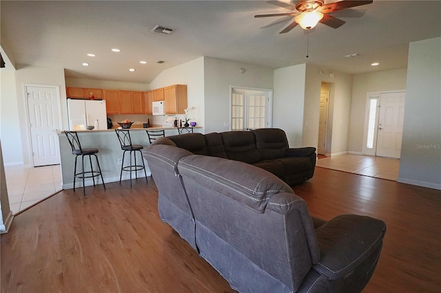 living room with vaulted ceiling, ceiling fan, and light wood-type flooring