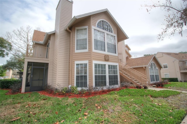 rear view of property featuring a balcony, a chimney, a sunroom, a yard, and stairway