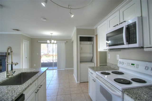 kitchen featuring white appliances, stacked washer / drying machine, a sink, a chandelier, and white cabinetry