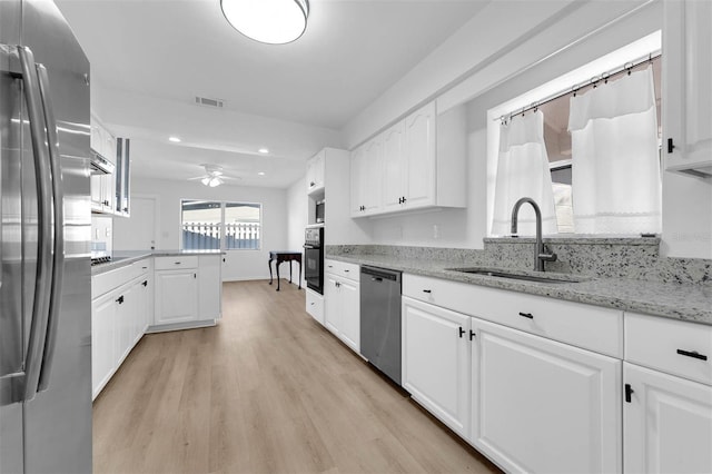 kitchen featuring visible vents, appliances with stainless steel finishes, white cabinetry, a sink, and light stone countertops