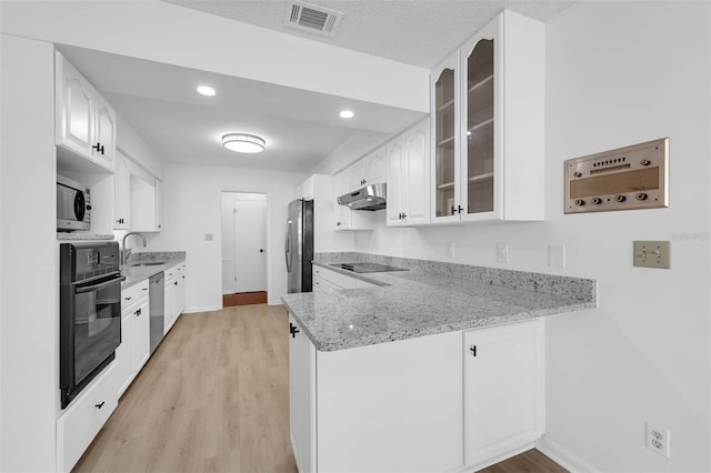 kitchen with light stone counters, under cabinet range hood, visible vents, black appliances, and glass insert cabinets