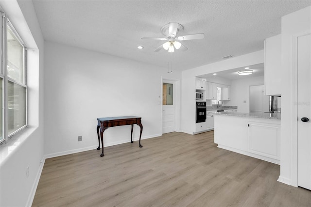 kitchen with light wood-style flooring, white cabinetry, black oven, light stone countertops, and stainless steel microwave