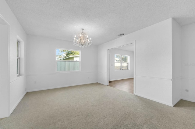 unfurnished room with a textured ceiling, carpet flooring, visible vents, and a notable chandelier