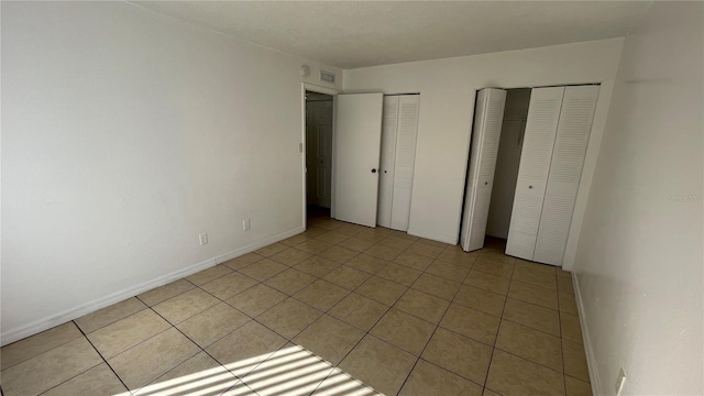 unfurnished bedroom with light tile patterned floors and multiple closets