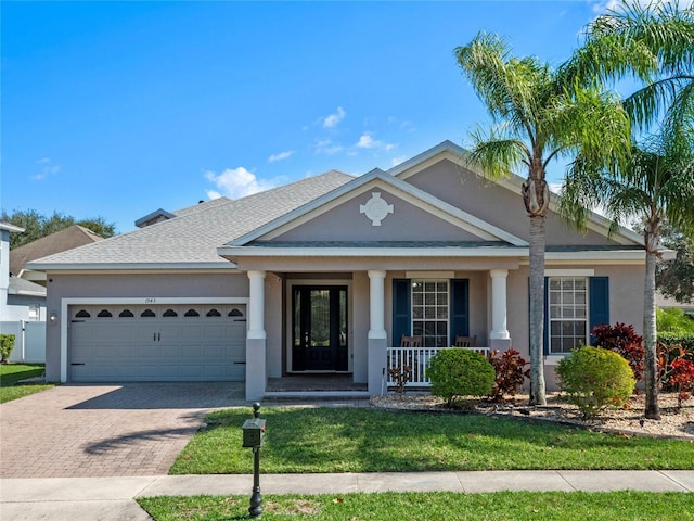 view of front of house featuring a porch, a garage, a shingled roof, decorative driveway, and stucco siding