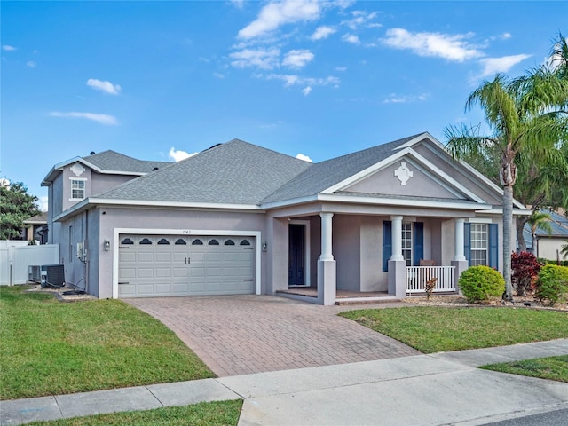 view of front of property featuring decorative driveway, stucco siding, central air condition unit, covered porch, and a front lawn