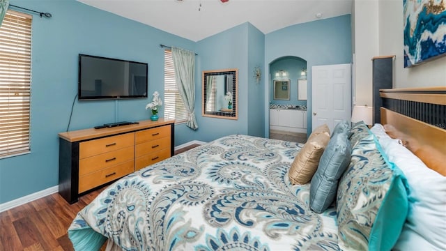 bedroom with dark wood-type flooring, ensuite bath, vaulted ceiling, and multiple windows