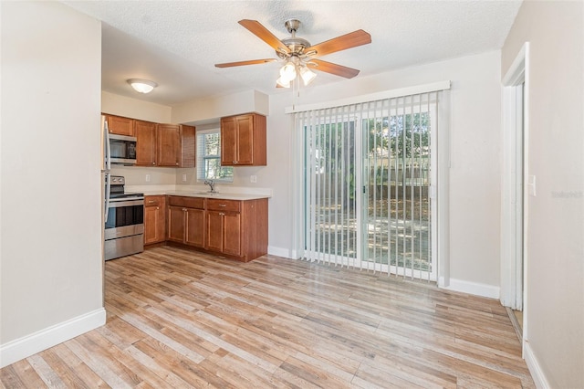 kitchen with appliances with stainless steel finishes, sink, ceiling fan, a textured ceiling, and light hardwood / wood-style flooring