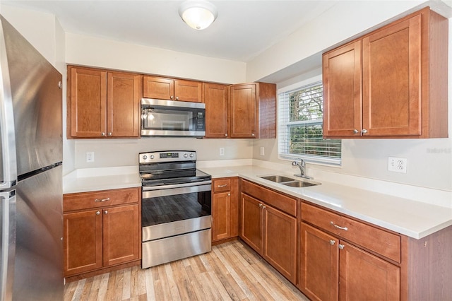 kitchen with appliances with stainless steel finishes, sink, and light wood-type flooring