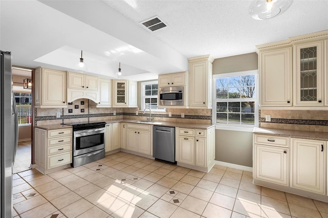 kitchen with tasteful backsplash, cream cabinets, and appliances with stainless steel finishes