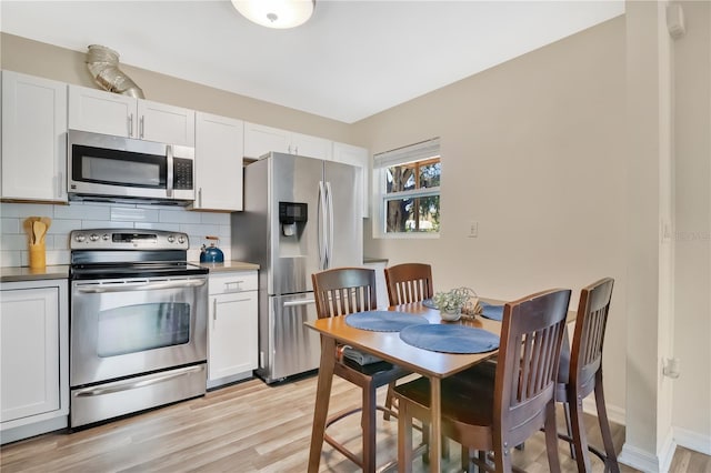 kitchen featuring white cabinetry, stainless steel appliances, light wood-type flooring, and backsplash