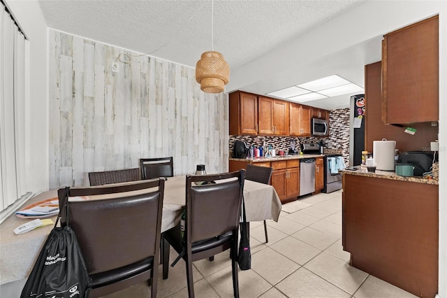 5201 Vineland Rd Unit 112, Orlando, FL 32811 - kitchen featuring tasteful backsplash, a textured ceiling, brown cabinetry, light tile patterned floors, and appliances with stainless steel finishes