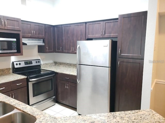 kitchen featuring stainless steel appliances, light tile patterned flooring, dark brown cabinets, and light stone counters