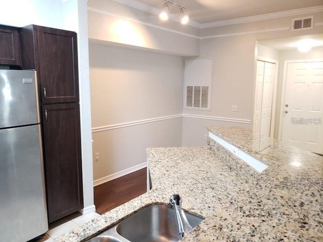 kitchen featuring stainless steel refrigerator, sink, ornamental molding, dark brown cabinetry, and light stone countertops