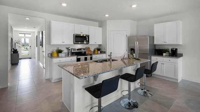 kitchen featuring appliances with stainless steel finishes, a breakfast bar area, a center island with sink, and white cabinets