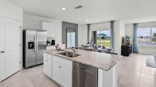 kitchen with appliances with stainless steel finishes, sink, white cabinets, a kitchen island with sink, and light stone counters