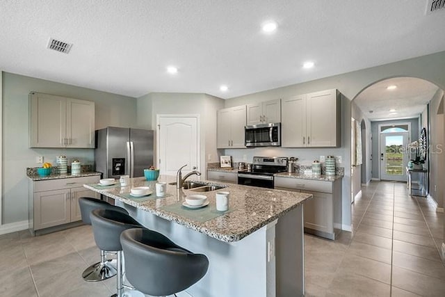 kitchen featuring gray cabinets, sink, a breakfast bar area, stainless steel appliances, and a center island with sink