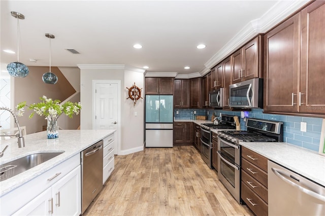 kitchen featuring hanging light fixtures, stainless steel appliances, light wood-style floors, white cabinetry, and a sink