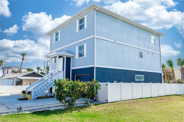 view of front of house featuring stairs, fence, a front lawn, and stucco siding