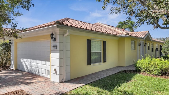 view of side of home with a tiled roof, an attached garage, and stucco siding