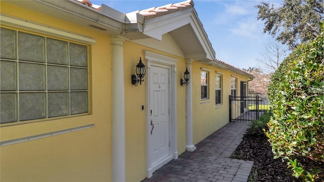 view of exterior entry featuring a tiled roof, a gate, and stucco siding