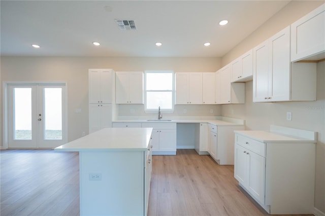 kitchen with sink, light hardwood / wood-style floors, white cabinets, a kitchen island, and french doors