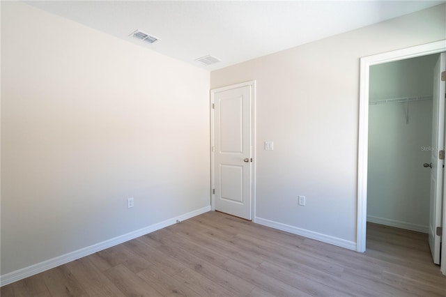 unfurnished bedroom with a closet, a spacious closet, and light hardwood / wood-style flooring