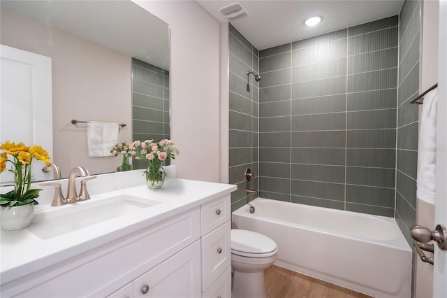 full bathroom with tiled shower / bath combo, vanity, hardwood / wood-style floors, and toilet