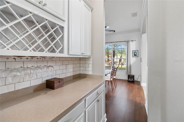 kitchen featuring crown molding, dark hardwood / wood-style floors, white cabinets, and decorative backsplash