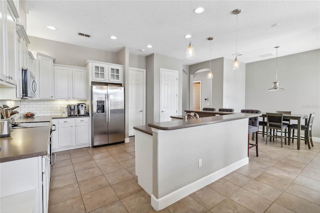 kitchen with white cabinets, backsplash, hanging light fixtures, a kitchen island with sink, and stainless steel appliances