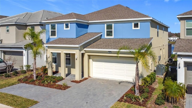 view of front of house featuring roof with shingles, stucco siding, central AC unit, a garage, and driveway