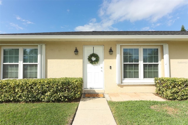 property entrance with a shingled roof, a lawn, and stucco siding