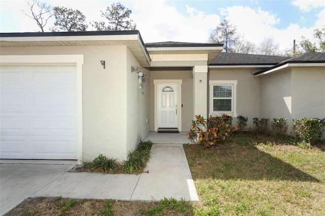 entrance to property featuring a garage, a lawn, and stucco siding