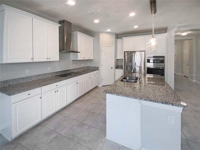 kitchen with sink, appliances with stainless steel finishes, an island with sink, wall chimney range hood, and white cabinets