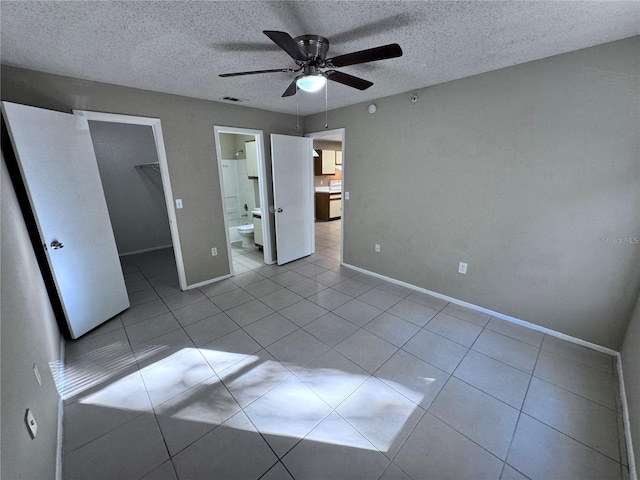 unfurnished bedroom with light tile patterned flooring, a walk in closet, a textured ceiling, a closet, and ceiling fan