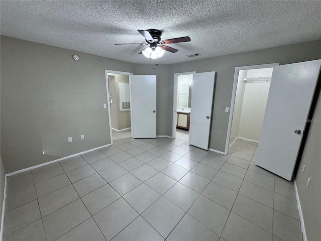 unfurnished bedroom featuring a walk in closet, a textured ceiling, light tile patterned floors, a closet, and ceiling fan